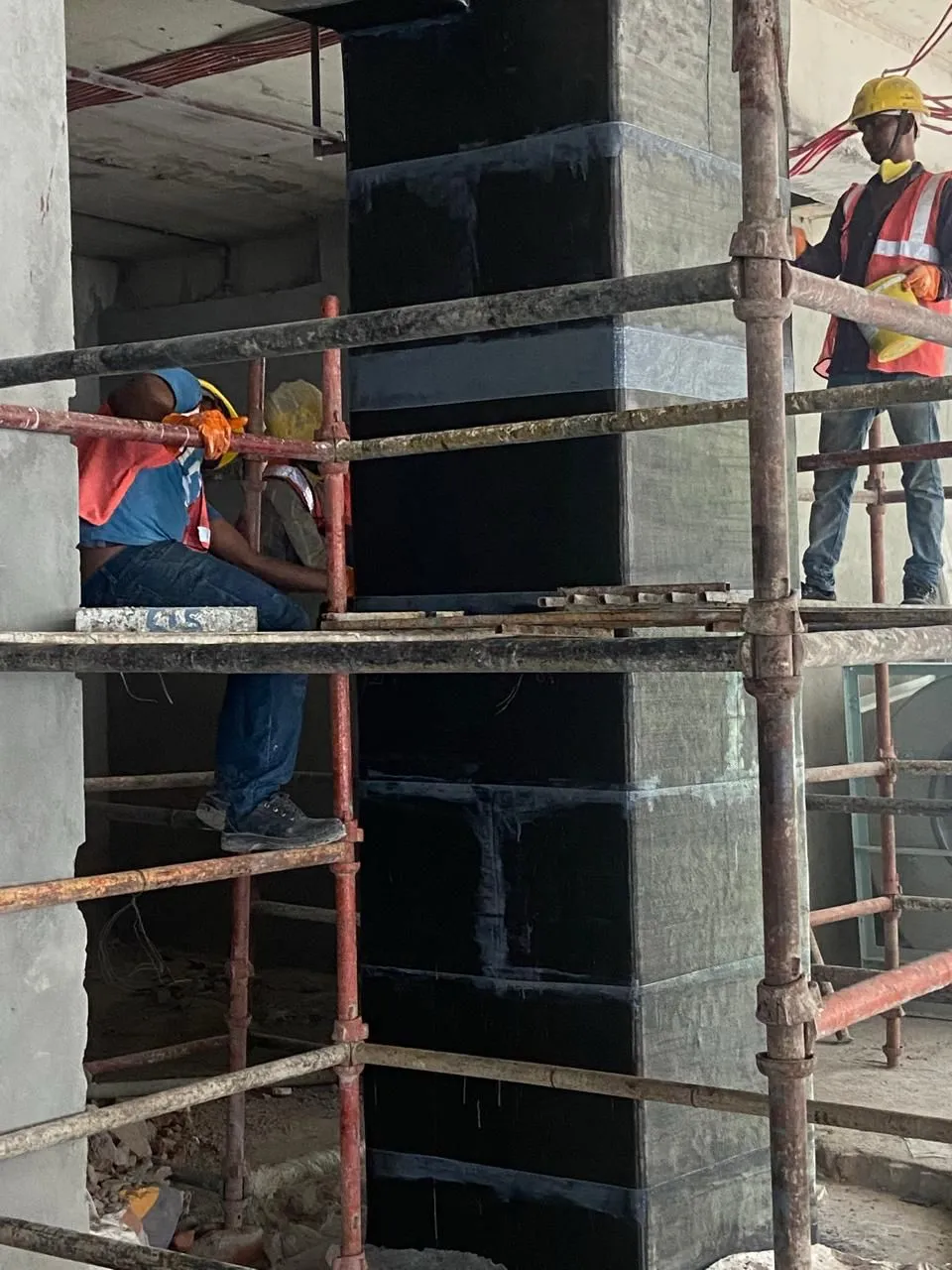 Workers on scaffolding wrapping a concrete column in black carbon fibre sheet