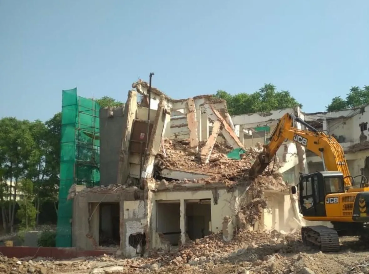 Excavator demolishing a multi-storey building with green safety netting
