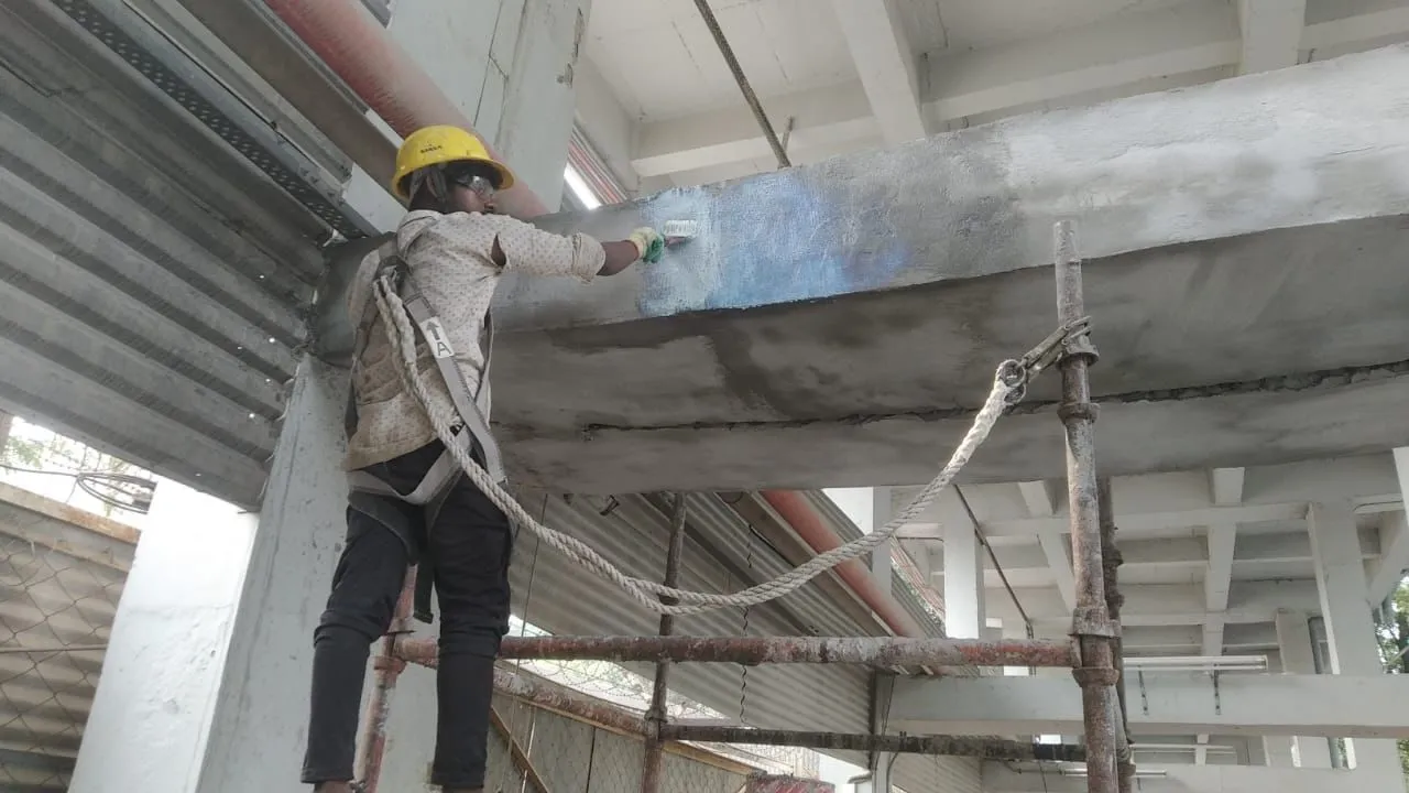 Worker on scaffolding applying coating to a repaired concrete beam